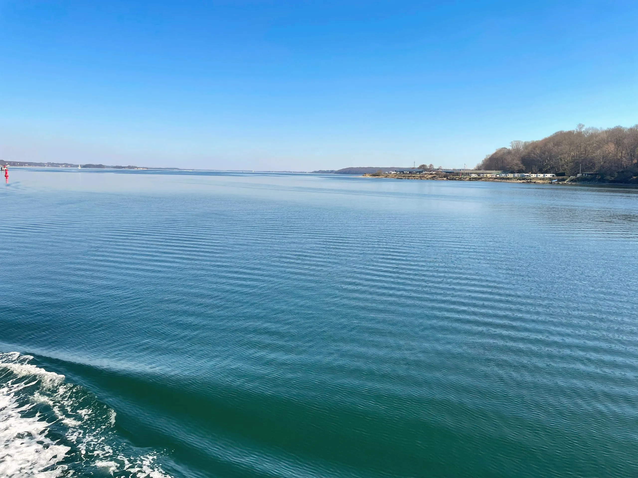 Blick vom Schiff über die blaue Förde auf die Landzunge